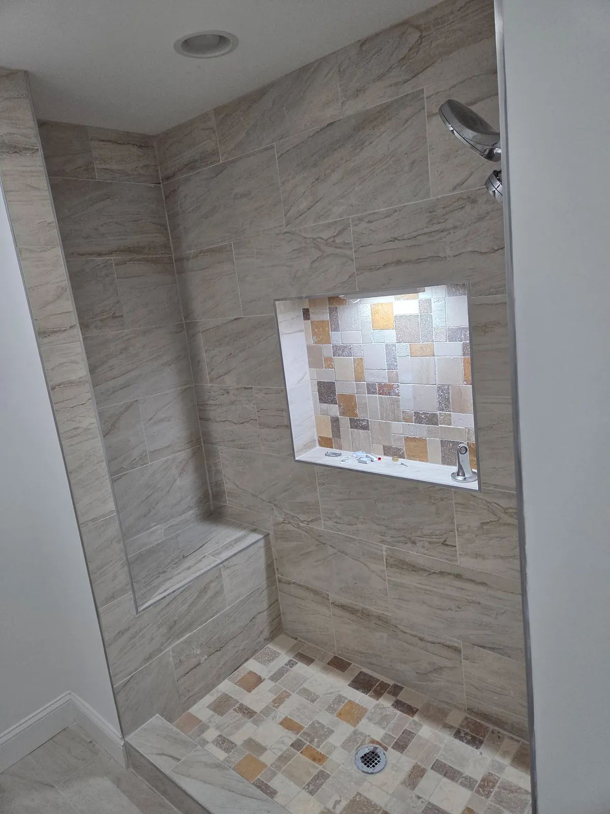Walk-in shower with large-format wall tile, a built-in bench, a lit niche, and mosaic tile floor