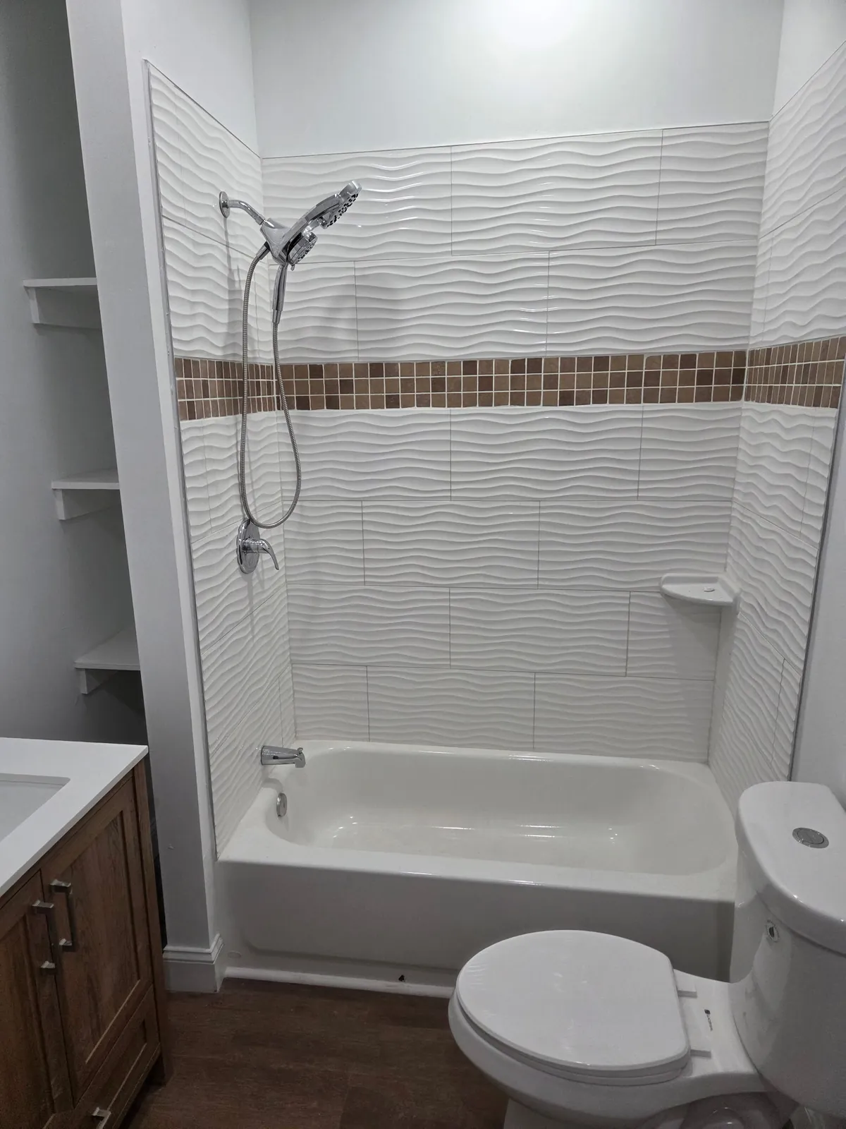 Tub surround in white wave tile with a mosaic accent band and built-in shelving
