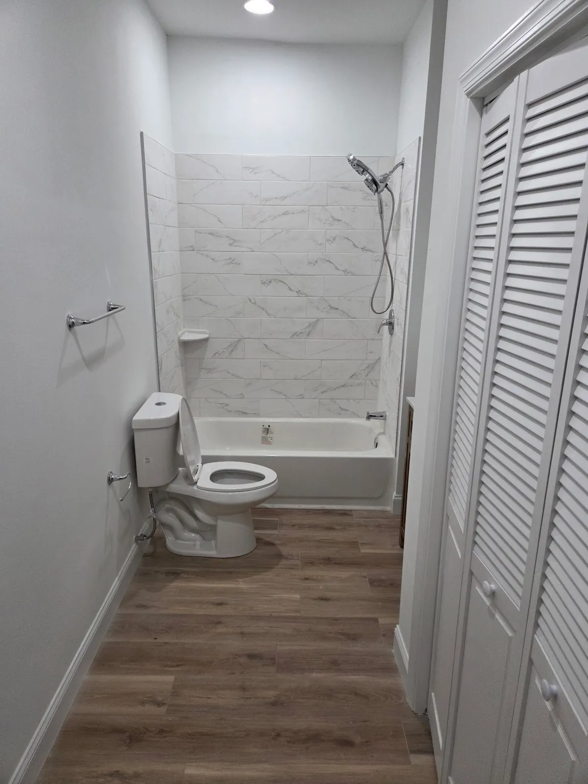 Bathroom with marble-look tile tub surround and wood-look flooring