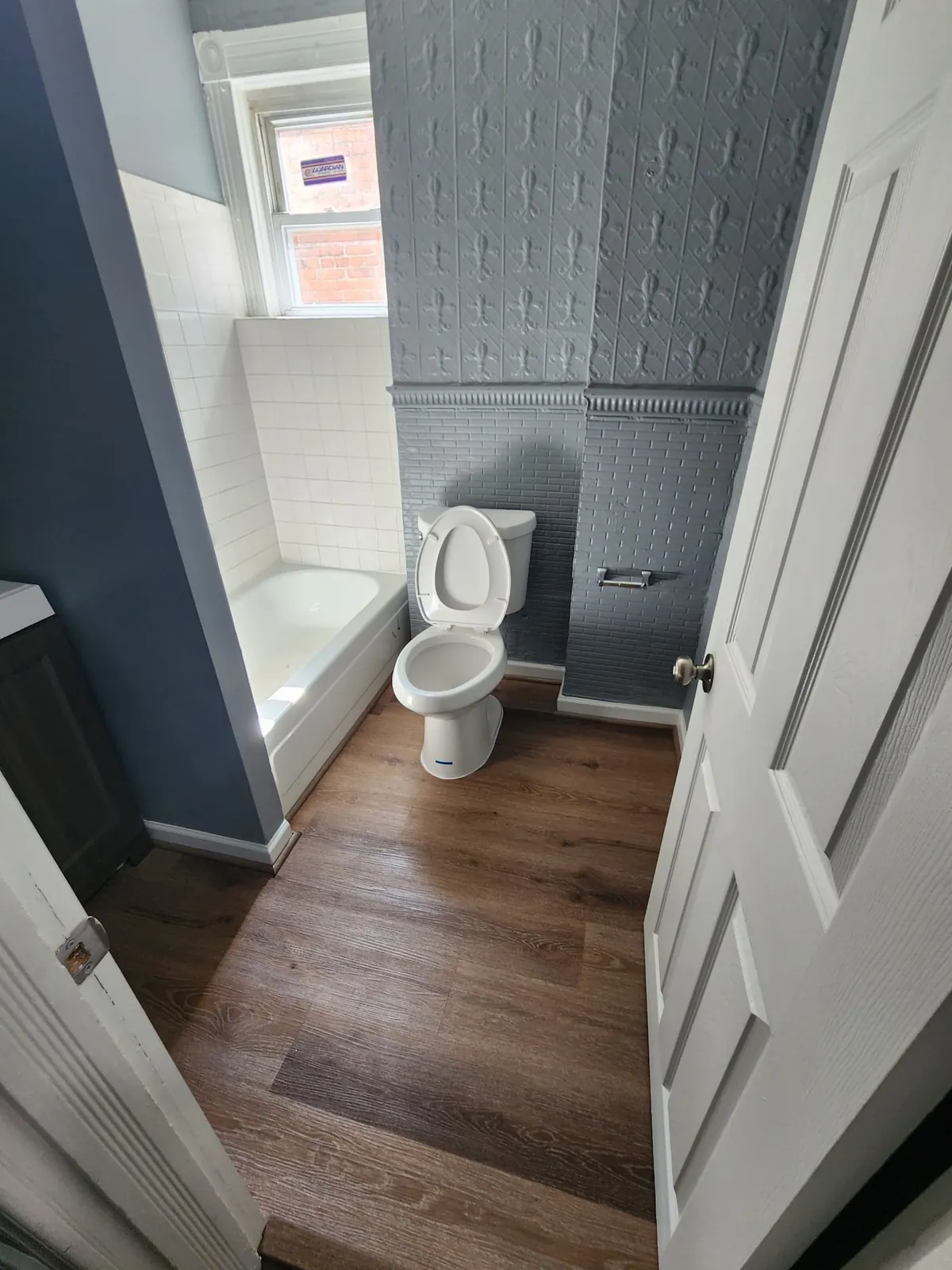 Bathroom with a restored pressed-tin accent wall, new tub, toilet, and wood-look flooring