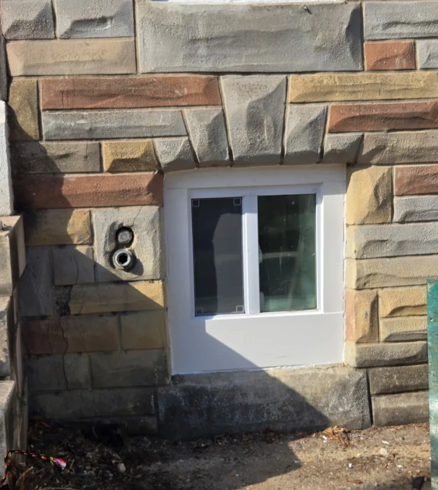 New white vinyl basement window set into a stone foundation wall