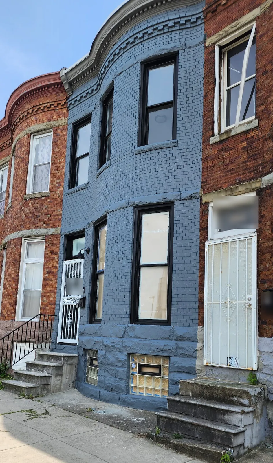Rowhouse with a freshly painted blue-gray brick facade, new black-framed windows, and a white security door