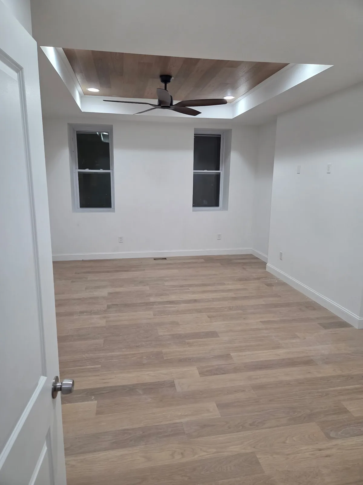 Bedroom with a tray ceiling, wood-plank ceiling inset, ceiling fan, and new plank flooring