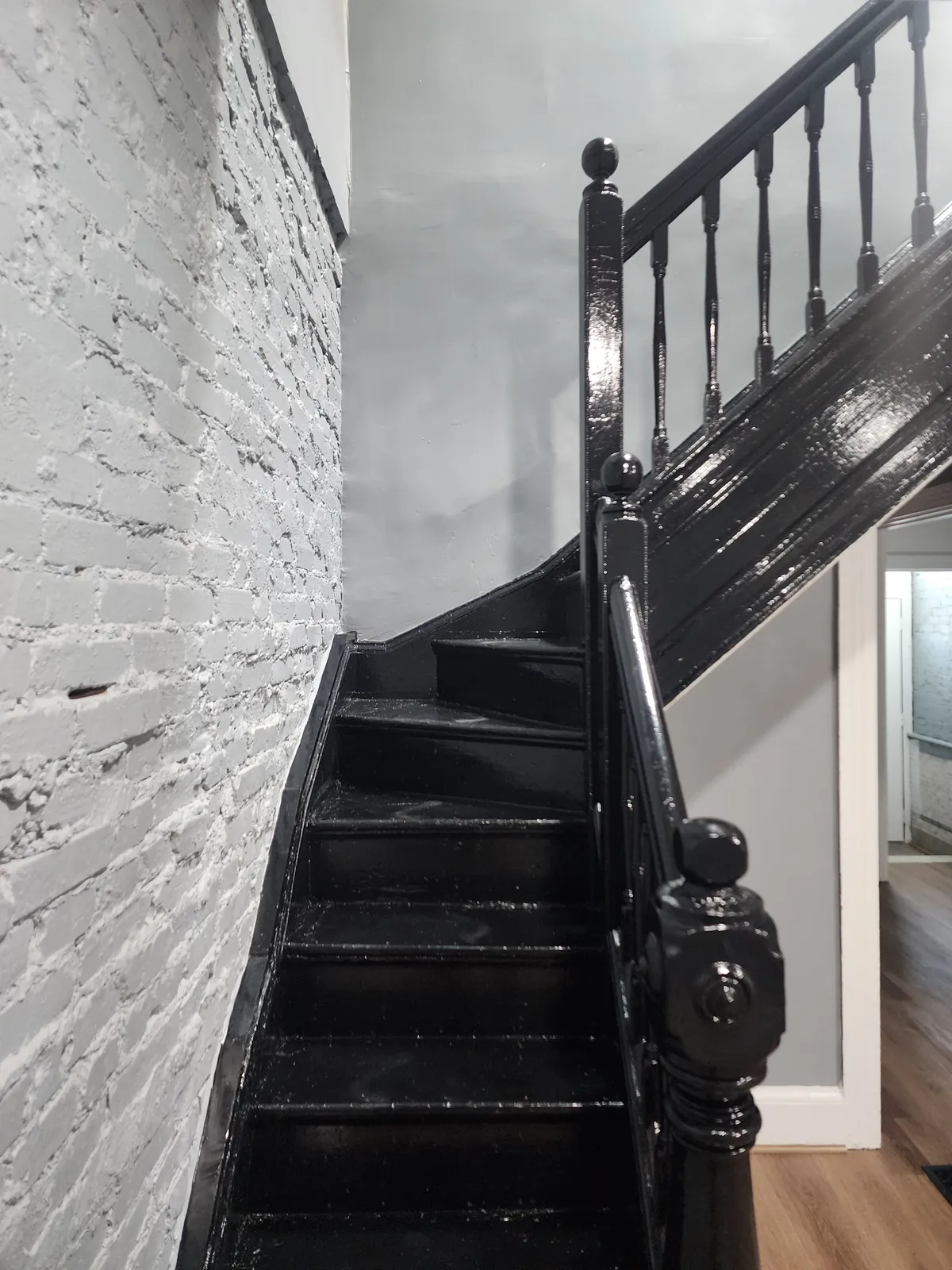 Refinished staircase and railing beside a painted exposed-brick wall