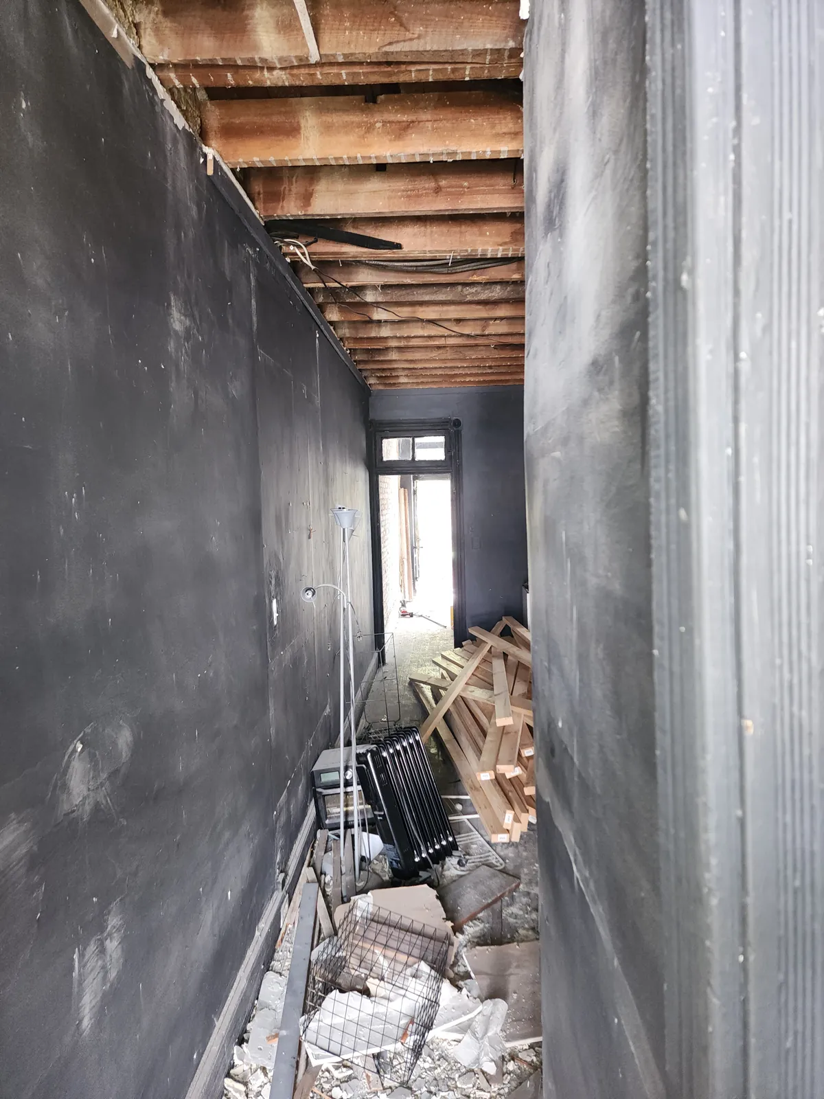 Before: hallway during demolition with open ceiling joists and debris