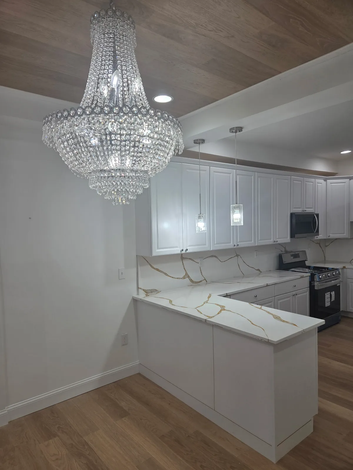 Renovated kitchen with white shaker cabinets, marble-look countertops, a crystal chandelier, and a wood-plank ceiling accent