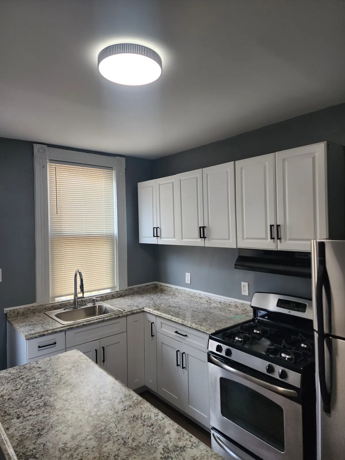 Compact kitchen with white cabinets, granite-look countertops, and stainless gas range