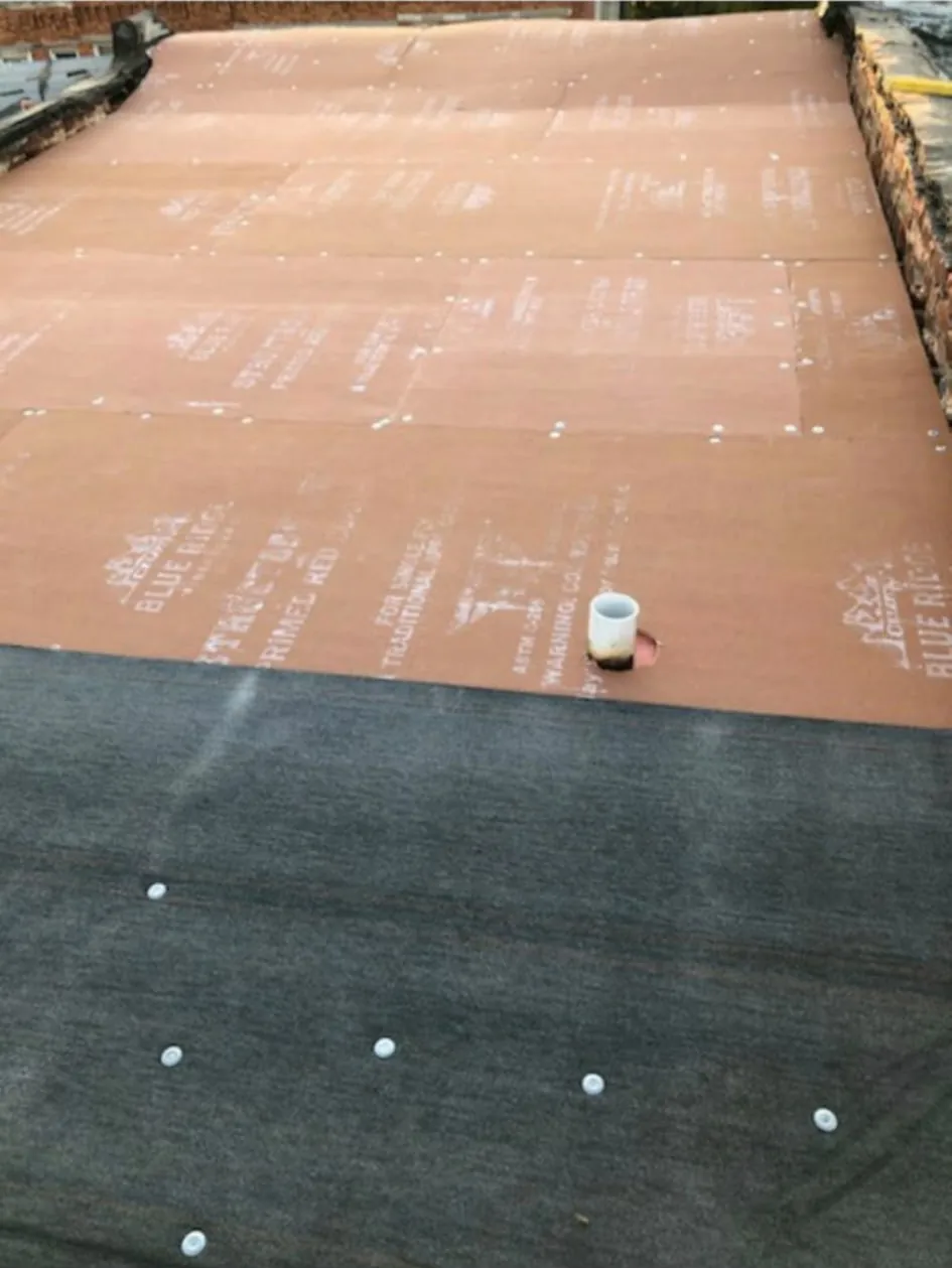 Another flat roof mid-install: red cover board over the deck with base sheet going down