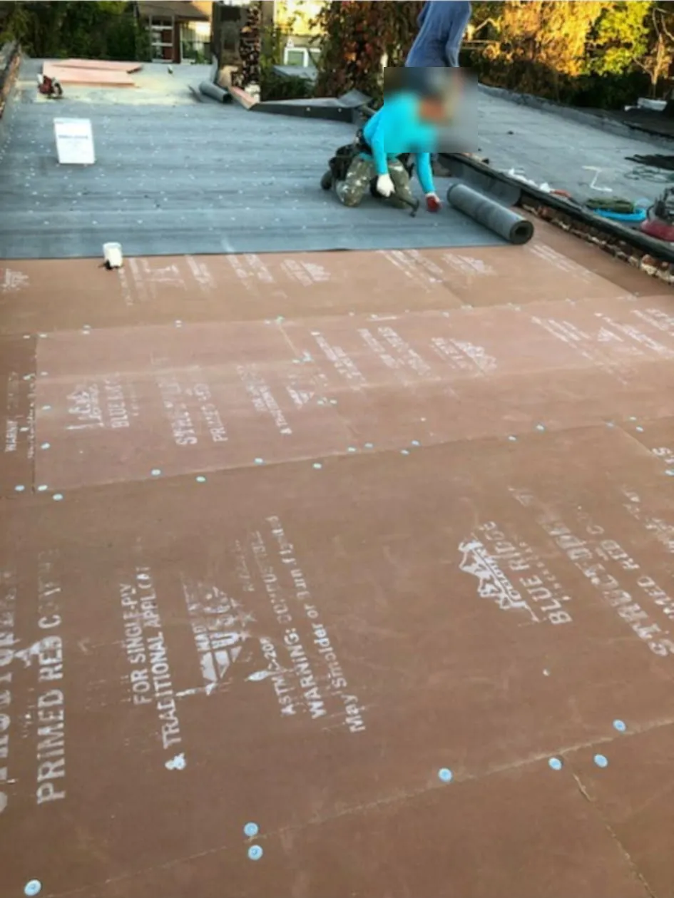 Crew member rolling out and fastening base sheet over cover board on a flat roof